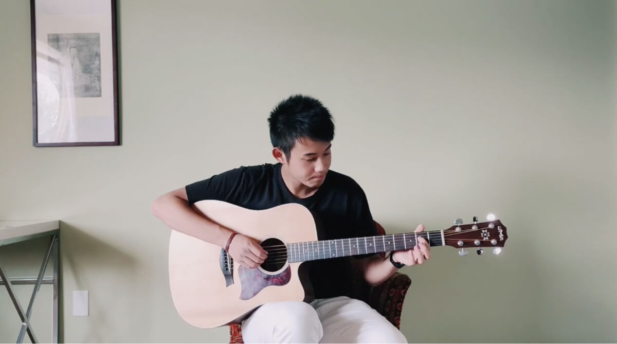 Guo playing guitar with a light green background.