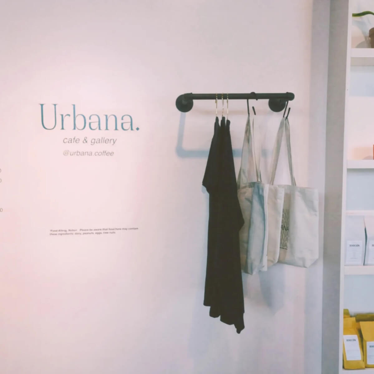 Sign of Urbana Cafe and hangers with tote bags and black t-shirts